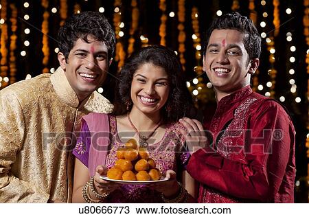 Stock Image - Portrait of two men and a woman holding sweets. Fotosearch