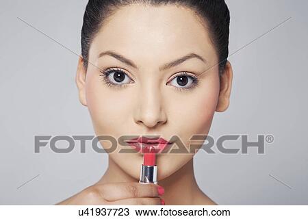 Stock Image - Portrait of woman applying lipstick . Fotosearch