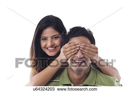 Stock Image - Portrait of woman covering mans eyes. Fotosearch