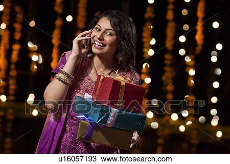 Stock Image - Portrait of woman with gifts talking on mobile phone. Fotosearch