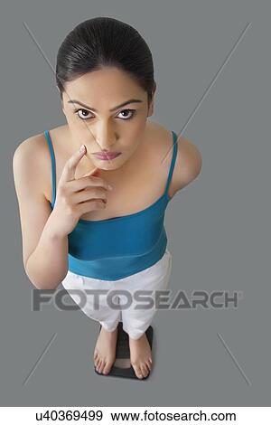Portrait of worried young woman standing on weighing scale isolated over gray background View Large Photo Image Stock Photo - Portrait of worried young woman standing on weighing scale isolated over gray background . Fotosearch