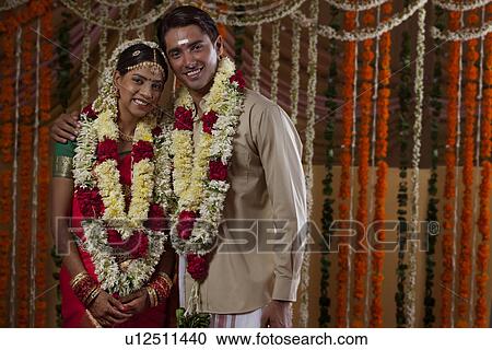 Stock Image - Portrait of young bride and groom wearing garlands during traditional Indian wedding . Fotosearch