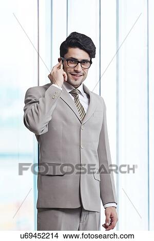 Portrait of young businessman answering smart phone in office View Large Photo Image Picture - Portrait of young businessman answering smart phone in office. Fotosearch