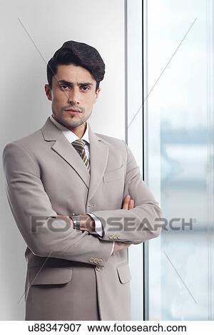 Stock Photo - Portrait of young businessman standing arms crossed in office. Fotosearch