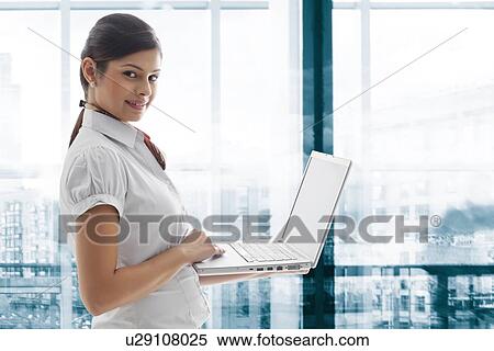 Stock Photography - Portrait of young businesswoman smiling with laptop at office . Fotosearch