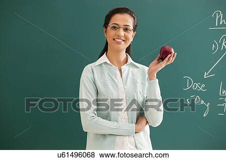 Portrait of young elementary school teacher holding an apple against green board View Large Photo Image Stock Photo - Portrait of young elementary school teacher holding an apple against green board . Fotosearch