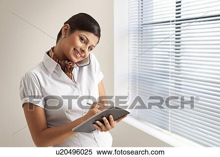 Stock Photography - Portrait of young executive writing business schedule while on phone call . Fotosearch