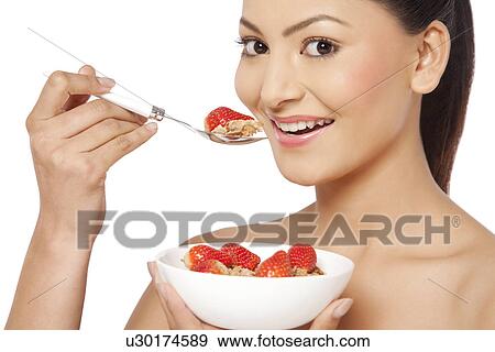 Stock Photo - Portrait of young female eating cornflakes with strawberries . Fotosearch