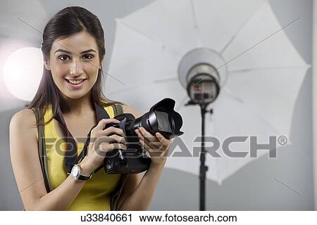 Stock Image - Portrait of young female photographer with digital camera in studio . Fotosearch