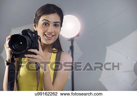 Stock Image - Portrait of young female photographer with digital camera in studio . Fotosearch