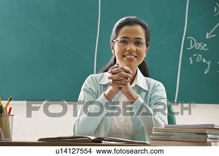 Picture - Portrait of young female teacher sitting at desk in classroom . Fotosearch