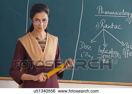 Stock Photograph - Portrait of young female teacher with attitude holding ruler against chalkboard . Fotosearch