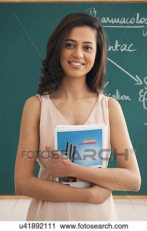 Portrait of young teacher holding books against green board View Large Photo Image Stock Image - Portrait of young teacher holding books against green board . Fotosearch
