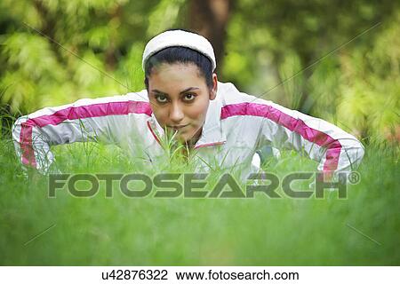 Stock Image - Portrait of young woman doing push-up on grass . Fotosearch