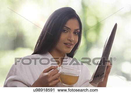 Portrait of young woman holding newspaper while drinking tea View Large Photo Image Stock Image - Portrait of young woman holding newspaper while drinking tea . Fotosearch