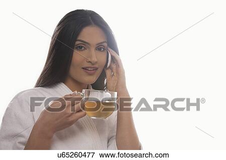 Stock Photo - Portrait of young woman holding tea cup while using mobile phone . Fotosearch