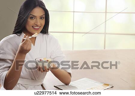 Portrait of young woman in bathrobe having breakfast at dining table View Large Photo Image Picture - Portrait of young woman in bathrobe having breakfast at dining table . Fotosearch