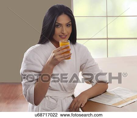 Portrait of young woman in bathrobe drinking orange juice at dining table  View Large Photo Image Stock Image - Portrait of young woman in bathrobe drinking orange juice at dining table . Fotosearch