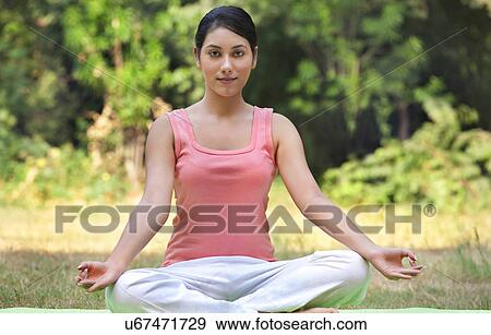 Stock Photo - Portrait of young woman in lawn sitting in lotus position . Fotosearch