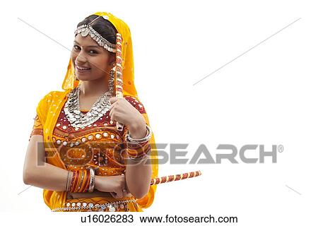 Stock Image - Portrait of young woman in traditional wear holding dandiyas isolated over white background. Fotosearch