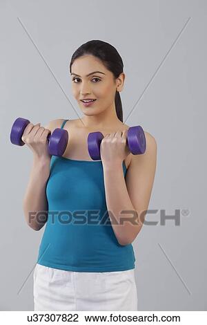 Portrait of young woman lifting dumbbells against gray background View Large Photo Image Stock Image - Portrait of young woman lifting dumbbells against gray background . Fotosearch