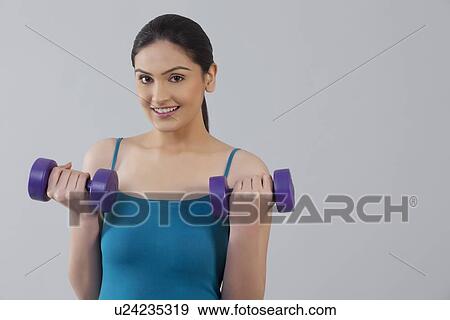 Portrait of young woman lifting dumbbells isolated over gray background View Large Photo Image Stock Photo - Portrait of young woman lifting dumbbells isolated over gray background . Fotosearch