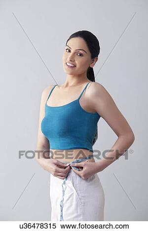 Stock Photography - Portrait of young woman measuring waist isolated over gray background . Fotosearch
