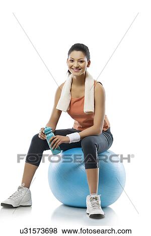 Stock Photo - Portrait of young woman sitting on a fitness ball after workout over white background . Fotosearch