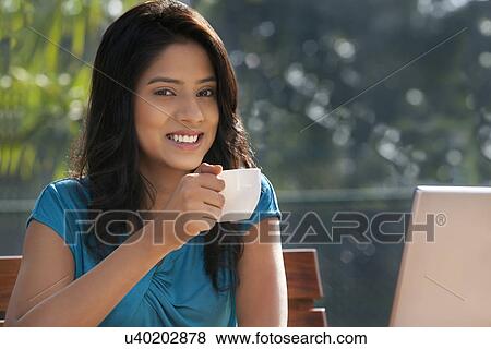 Stock Photo - Portrait of young woman smiling while having coffee . Fotosearch