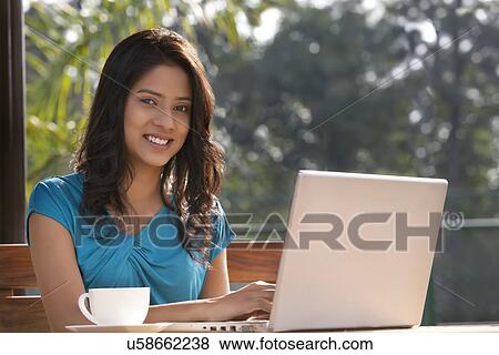 Stock Photo - Portrait of young woman smiling while using laptop . Fotosearch