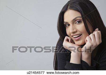 Portrait of young woman smiling with hand on chin over colored background View Large Photo Image Stock Photo - Portrait of young woman smiling with hand on chin over colored background . Fotosearch