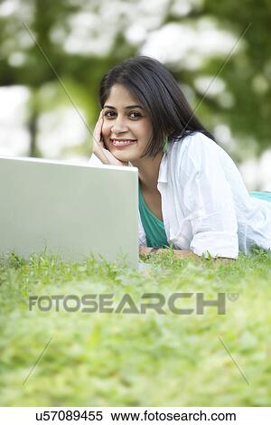 Portrait of young woman using laptop while lying on grass View Large Photo Image Stock Photography - Portrait of young woman using laptop while lying on grass . Fotosearch