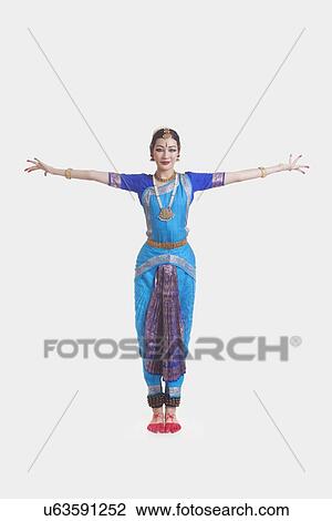 Stock Image - Portrait of young woman with arms outstretched performing Bharatanatyam against white background. Fotosearch