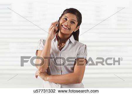 Stock Image - Pretty young business woman smiling while attending phone call . Fotosearch