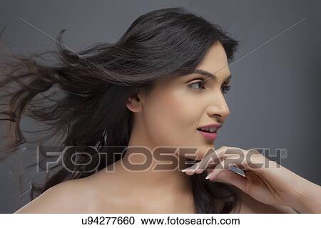 Stock Image - Pretty young female looking away with hair blowing over colored background . Fotosearch