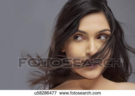 Pretty young female with hair blowing over face against colored background View Large Photo Image Stock Photo - Pretty young female with hair blowing over face against colored background . Fotosearch