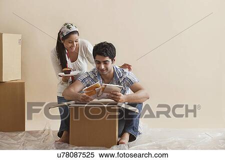 Stock Photography - Pretty young woman holding cupcake while man busy looking at magazines . Fotosearch