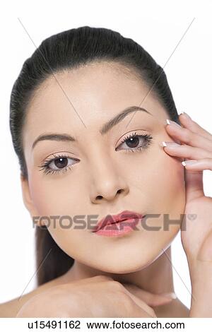 Stock Image - Pretty young woman touching her face over white background . Fotosearch