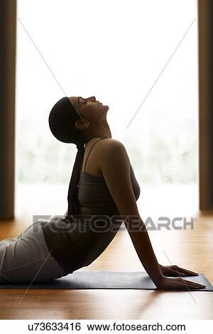Stock Photograph - Profile shot of young woman doing yogic 'sun salutation' on mat. Fotosearch