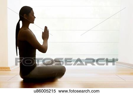 Stock Photography - Profile shot of young woman meditating on hardwood floor. Fotosearch