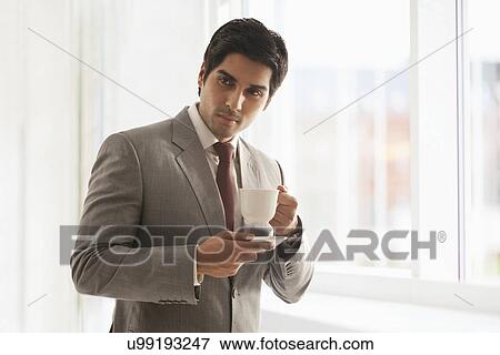 Proud young businesswoman having cup of coffee at office View Large Photo Image Stock Photo - Proud young businesswoman having cup of coffee at office . Fotosearch