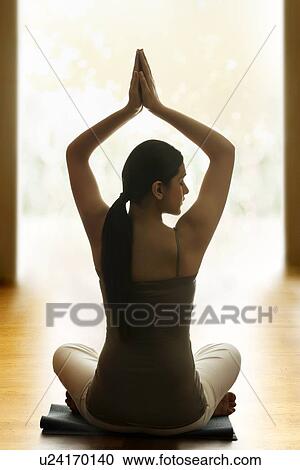 Stock Image - Rear view of woman meditating on floor. Fotosearch