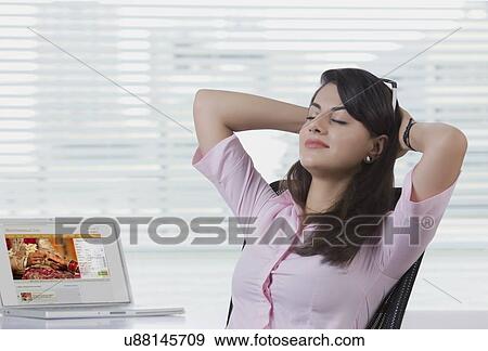 Relaxed businesswoman sitting with laptop at desk in office View Large Photo Image Stock Photo - Relaxed businesswoman sitting with laptop at desk in office. Fotosearch