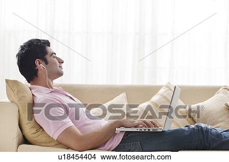 Relaxed man enjoying music with eyes closed on sofa View Large Photo Image Picture - Relaxed man enjoying music with eyes closed on sofa . Fotosearch