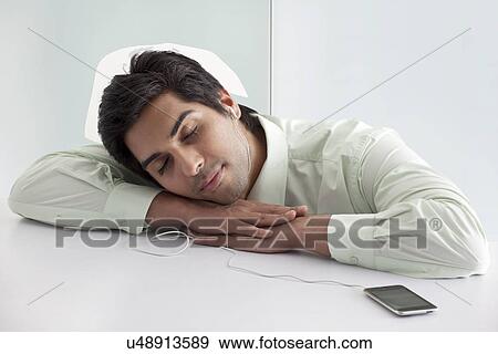 Stock Photo - Relaxed young businessman listening music through cell phone . Fotosearch