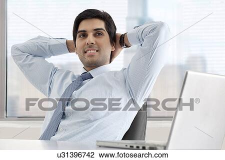 Stock Image - Relaxed young businessman sitting at his desk with laptop . Fotosearch
