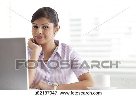 Stock Photo - Relaxed young businesswoman sitting at her desk . Fotosearch