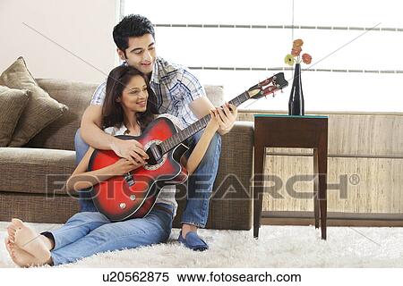 Stock Photography - Relaxed young couple playing guitar together at home . Fotosearch