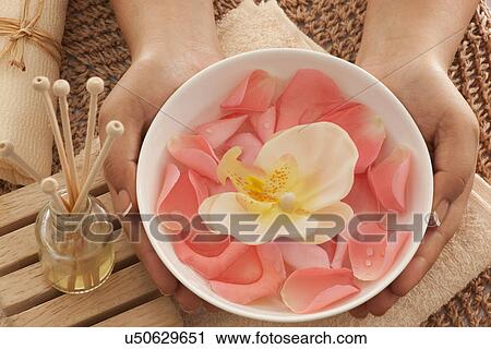 Stock Image - Rose petals and orchid in a bowl with reed diffuser . Fotosearch