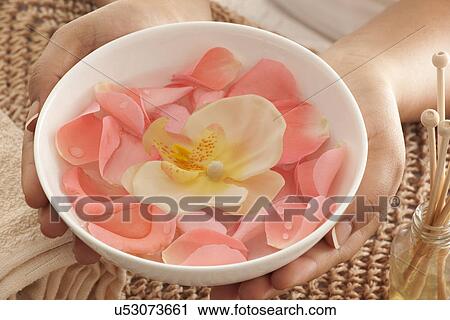 Stock Image - Rose petals and orchid in a bowl with reed diffuser . Fotosearch